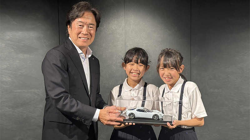 Akio Toyoda mit zwei Mädchen, die ein weißes Modellauto präsentieren