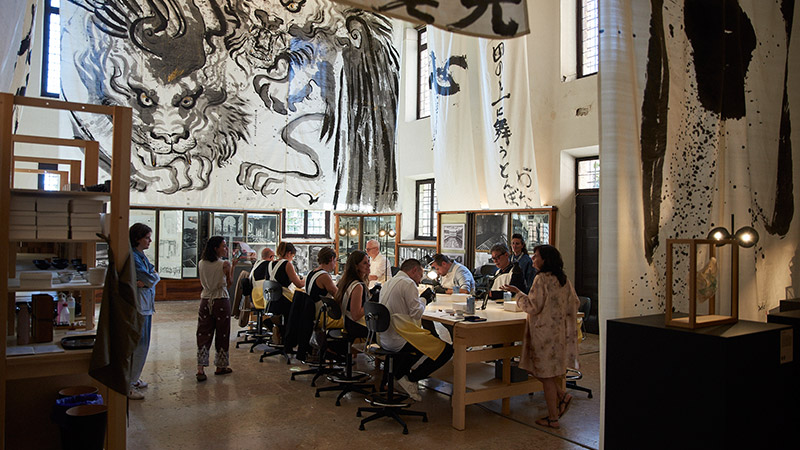 Menschen arbeiten in einem Atelier mit japanischer Kalligrafie an den Wänden